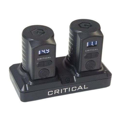 The image shows a Critical XR power supply unit with two digital displays, each showing different voltage readings. The unit is black, compact, and features a dual setup, allowing for the simultaneous monitoring and adjustment of power output for tattoo machines. The Critical logo is prominently displayed on the base of the unit.